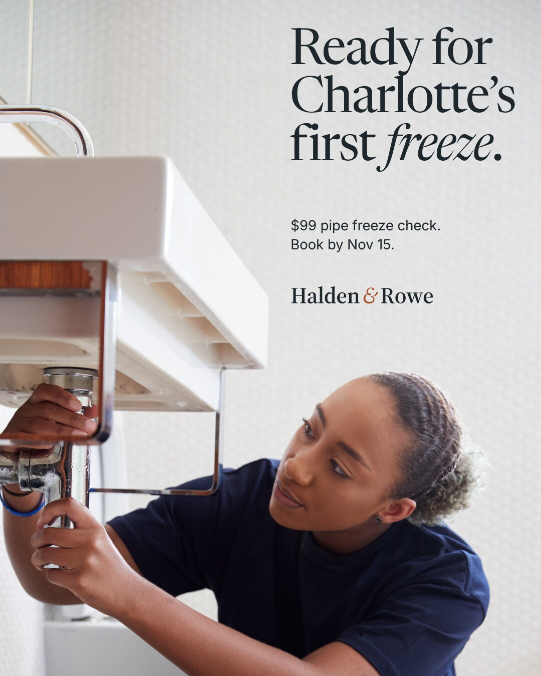 Concept brand: Halden & Rowe (fictional). A plumber in a navy tee works on the pipes under a bathroom sink. Text on the white wall reads: Ready for Charlotte's first freeze. $99 pipe freeze check. Book by Nov 15. Halden & Rowe wordmark.