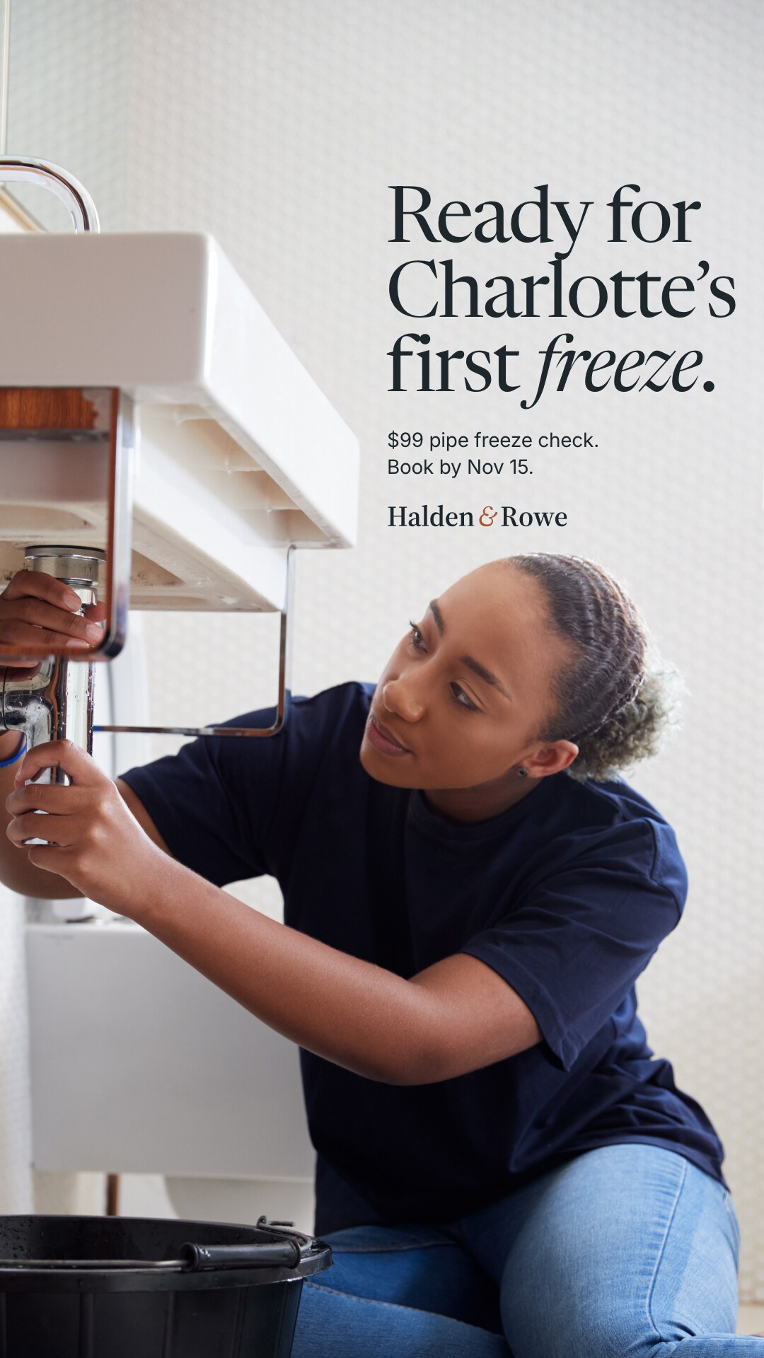 Concept brand: Halden & Rowe (fictional). A plumber sits on a bathroom floor, both hands on the pipes under the sink. Text on the white wall reads: Halden & Rowe wordmark. Ready for Charlotte's first freeze. $99 pipe freeze check. Book by Nov 15.
